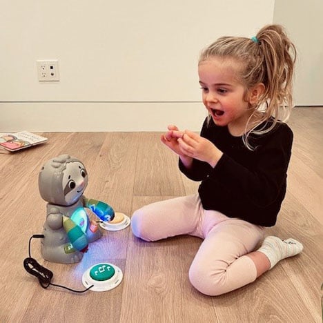 A young girl in a black shirt and pink leggings playing with a switch adapted toy sloth.