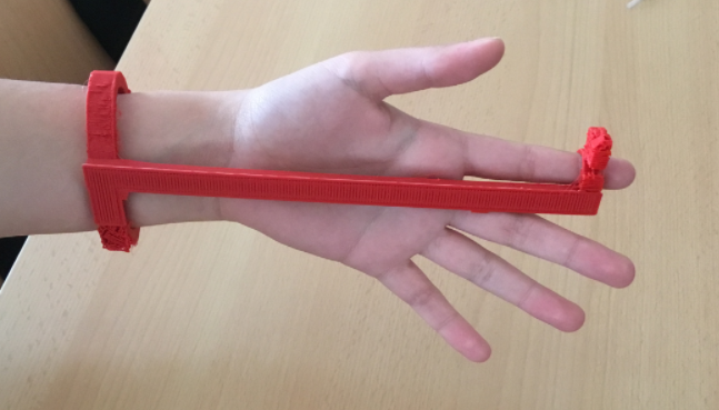 A red 3d printed arm mounted pen holder looped through the wrist and index finger.