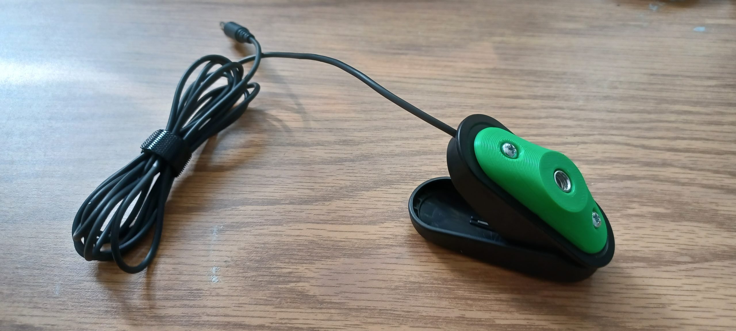 A green 3d printed adapted attached to Logitech's variable trigger button against a wooden background.