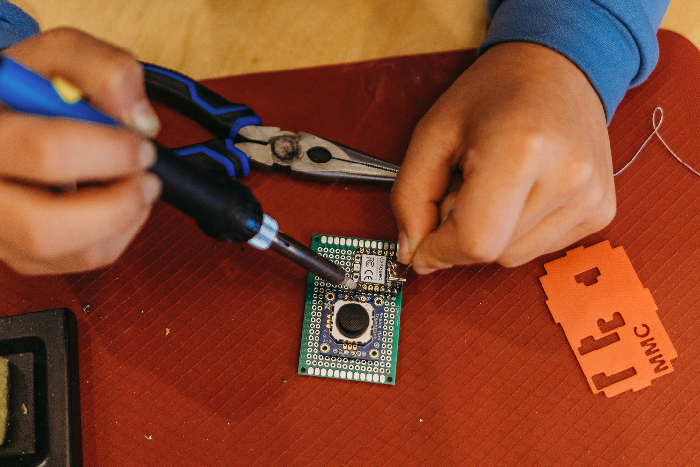 A pair of hands soldering electronic parts on a green PCB board