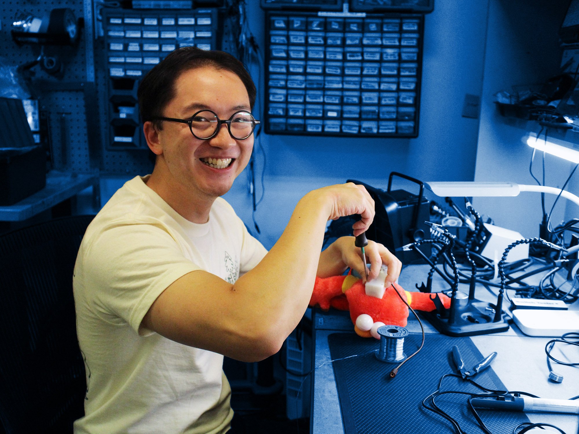 A man using a screwdriver to open a toy at an electronics workbench