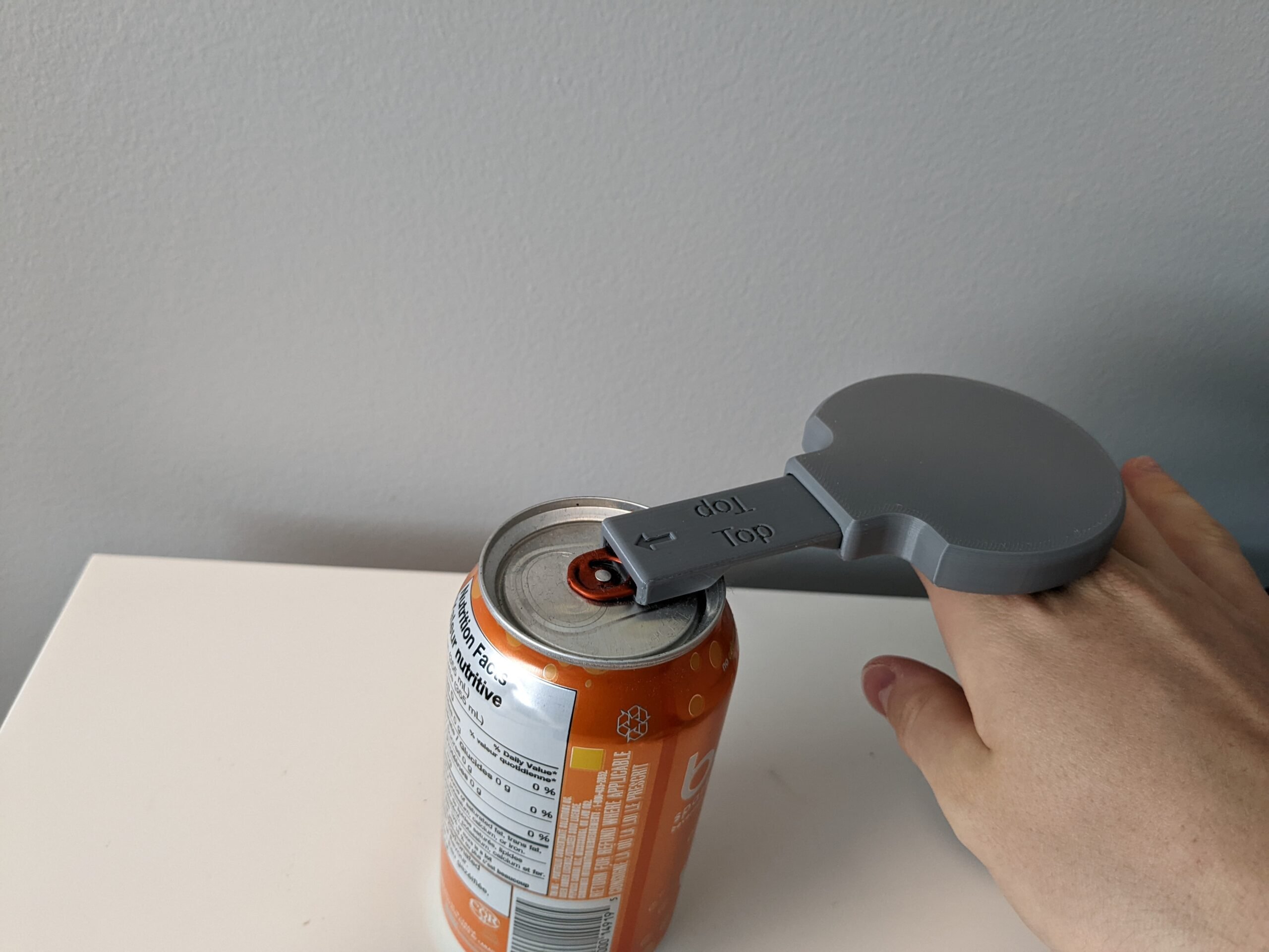 A hand holdinga 3d printed can opener with a flat handle to open a soda can.