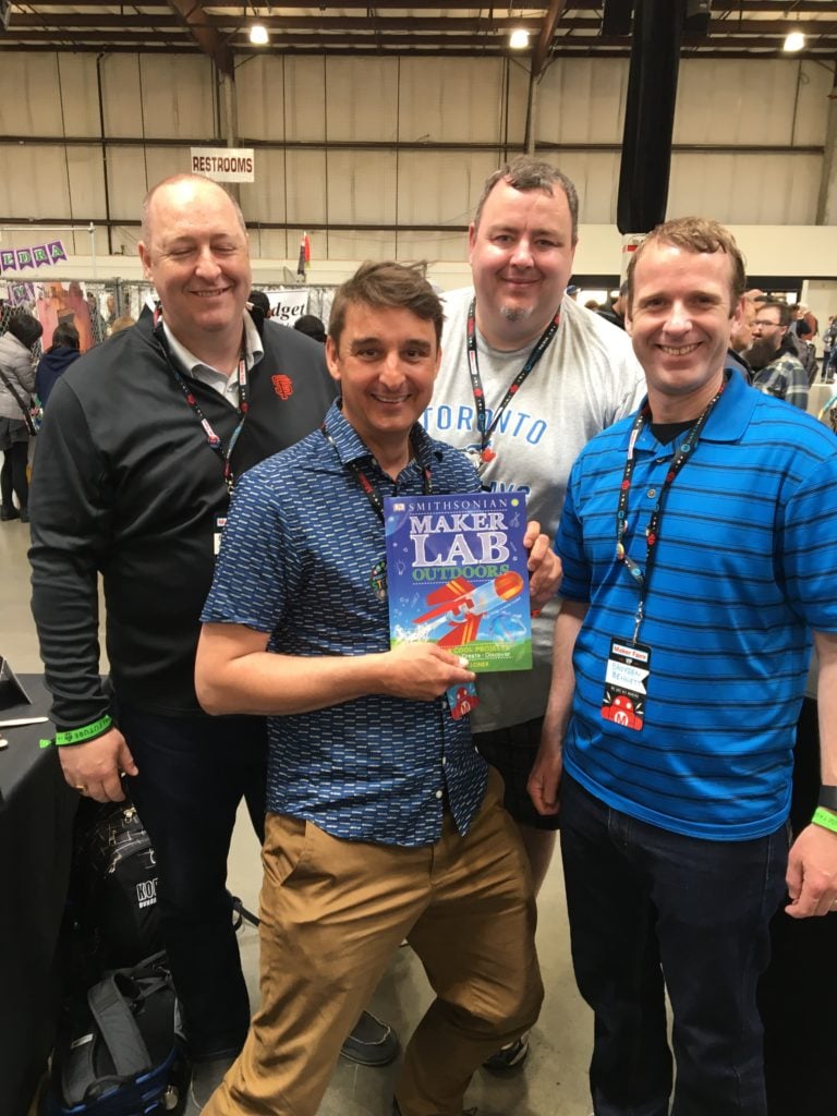 Four volunteers holding a book titled 'Maker Lab.'