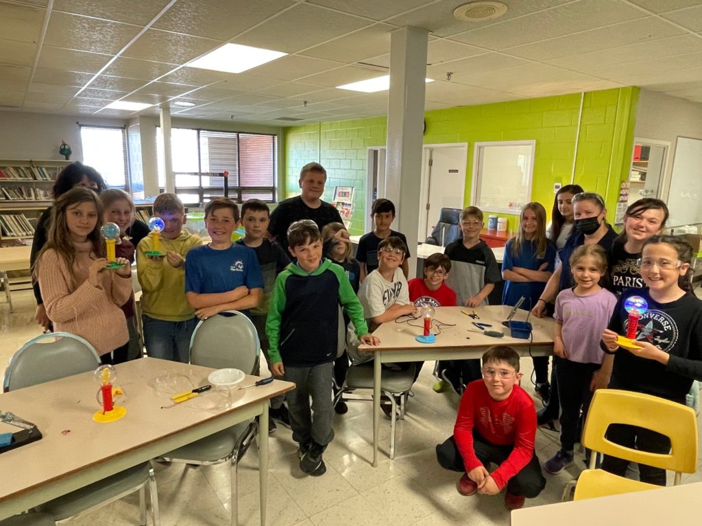 Students in a classroom smiling and holding up their switch-adapted toys.