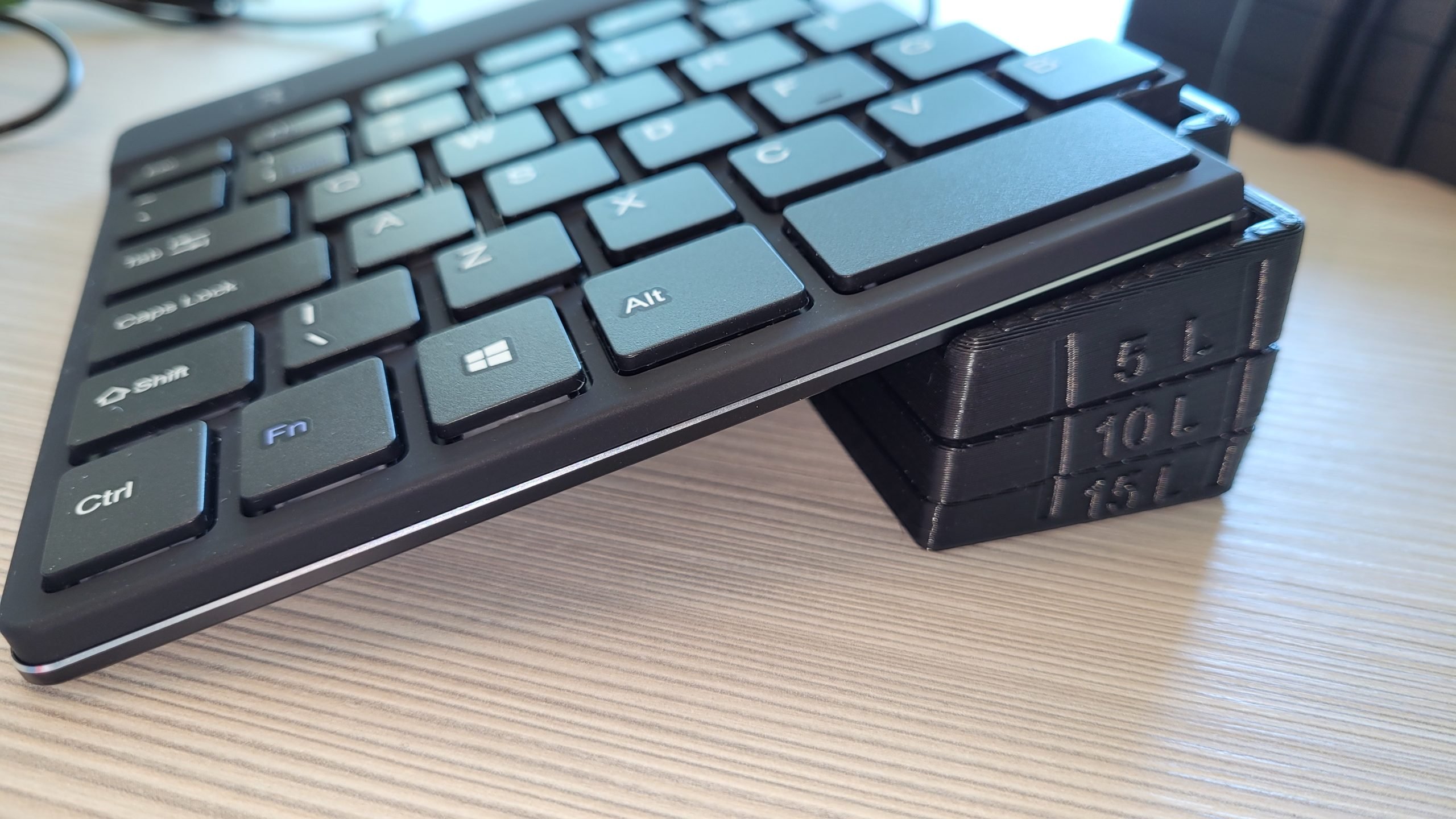 A picture of an R-Go Split Ergonomic Keyboard resting on 3D Printed blocks forming a 15-degree tenting angle.