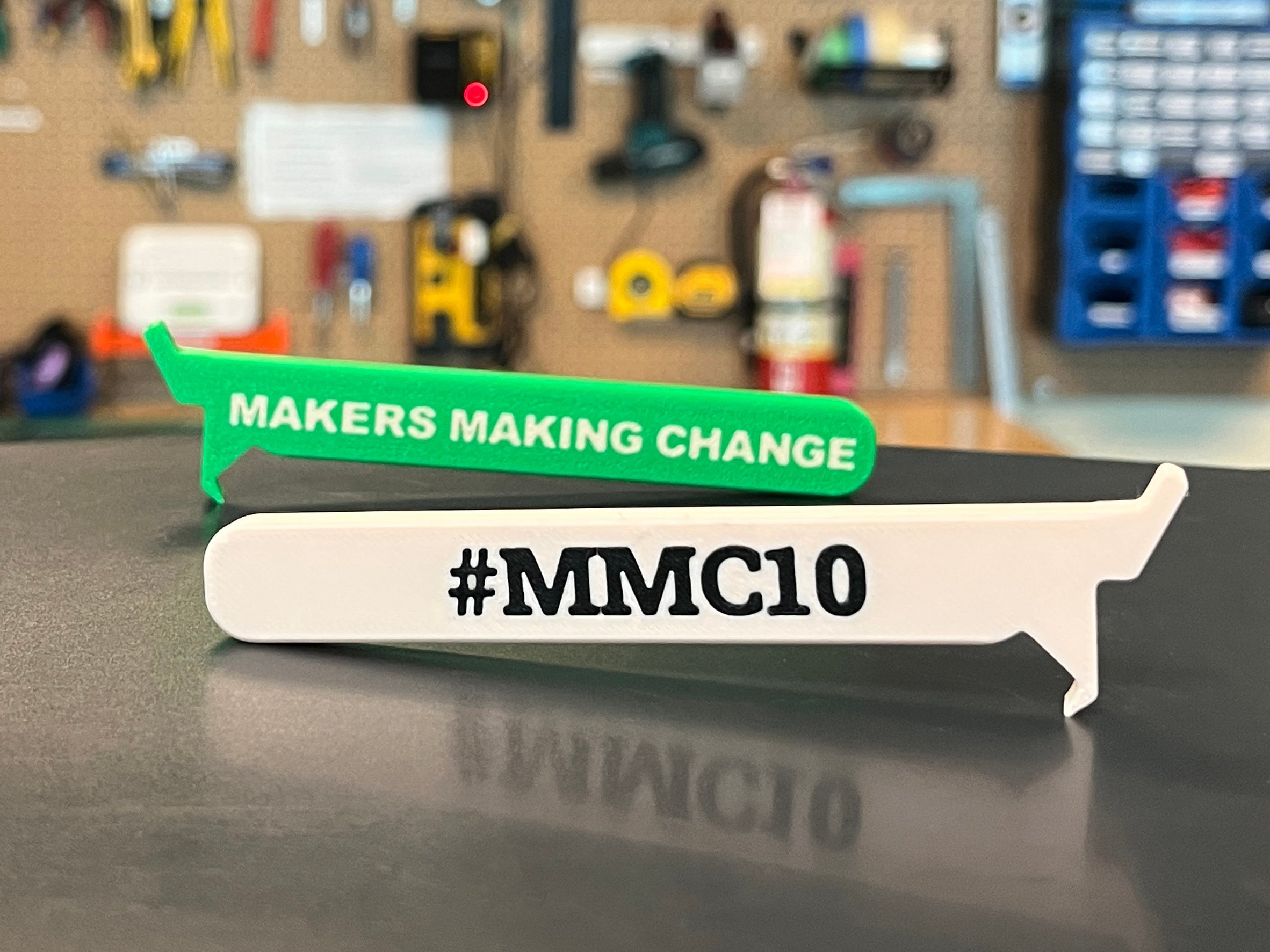 Two green and white 3d printed beverage can opener in front of a peg board of tools
