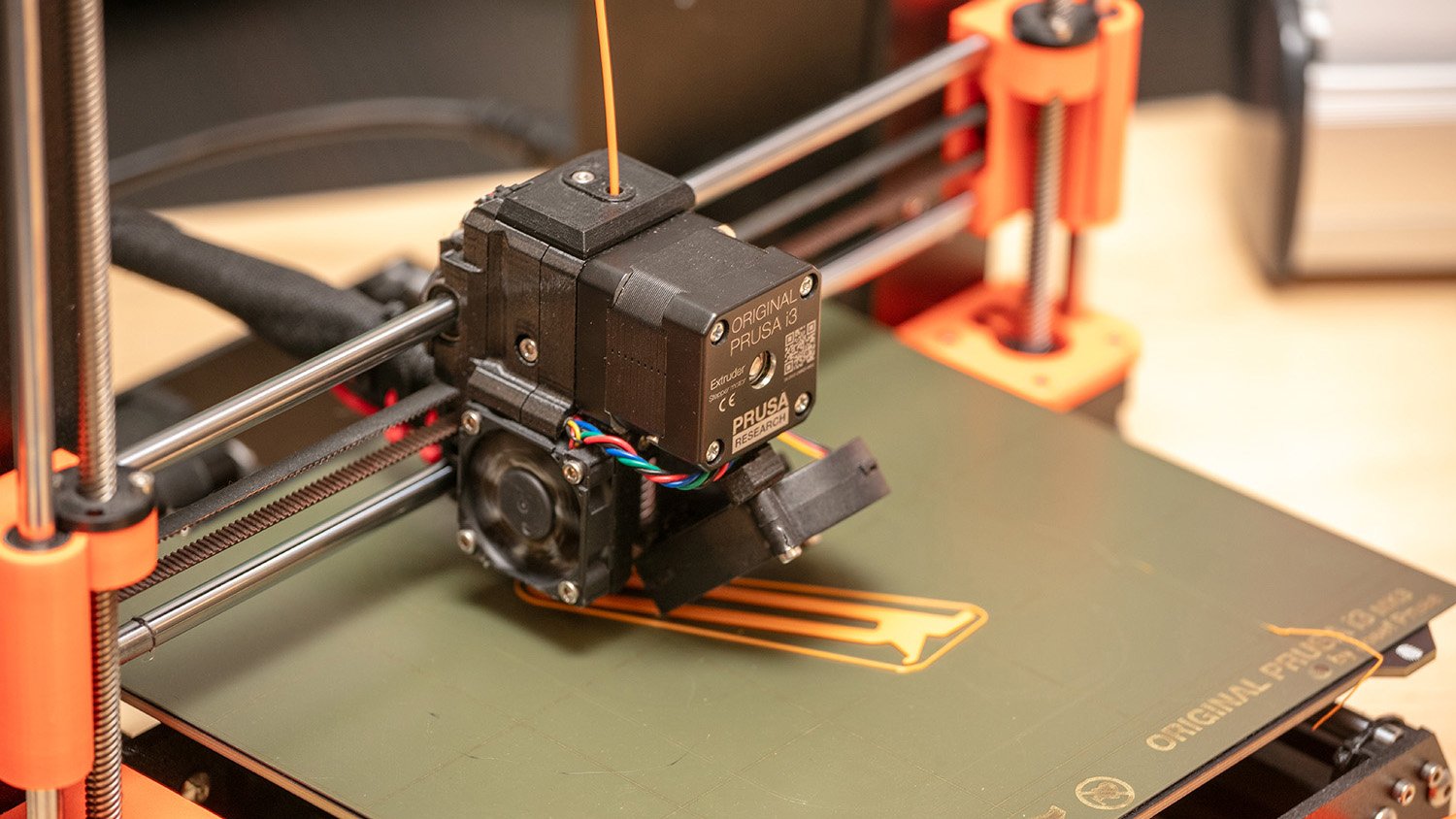 A Prusa 3D printer printing an orange assistive device.