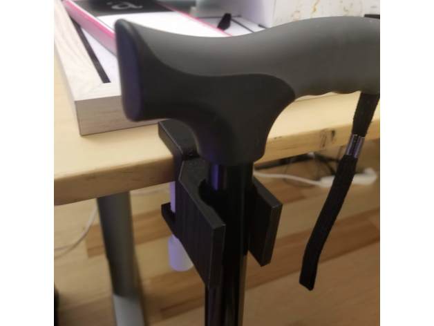 A black 3D printed cane holder attached to a table tha'ts holding a black cane.