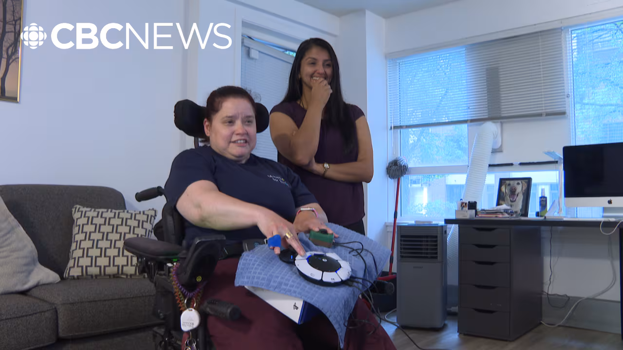 A gamer in a wheelchair using the PS5 Access Controller. Behind her is a staff
