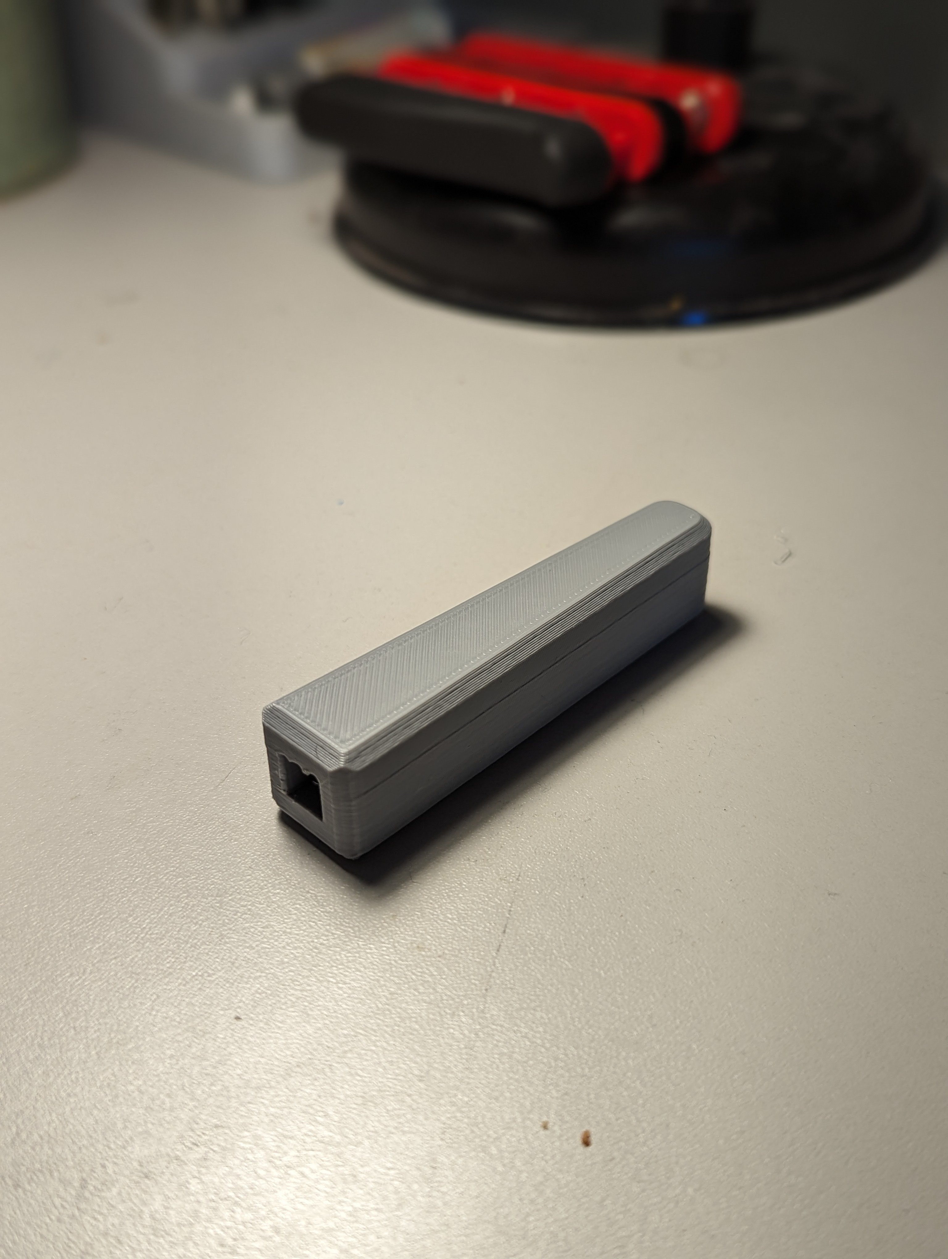 A great 3D printed light switch extension lever arm sitting on a white table with a black red device in the background.