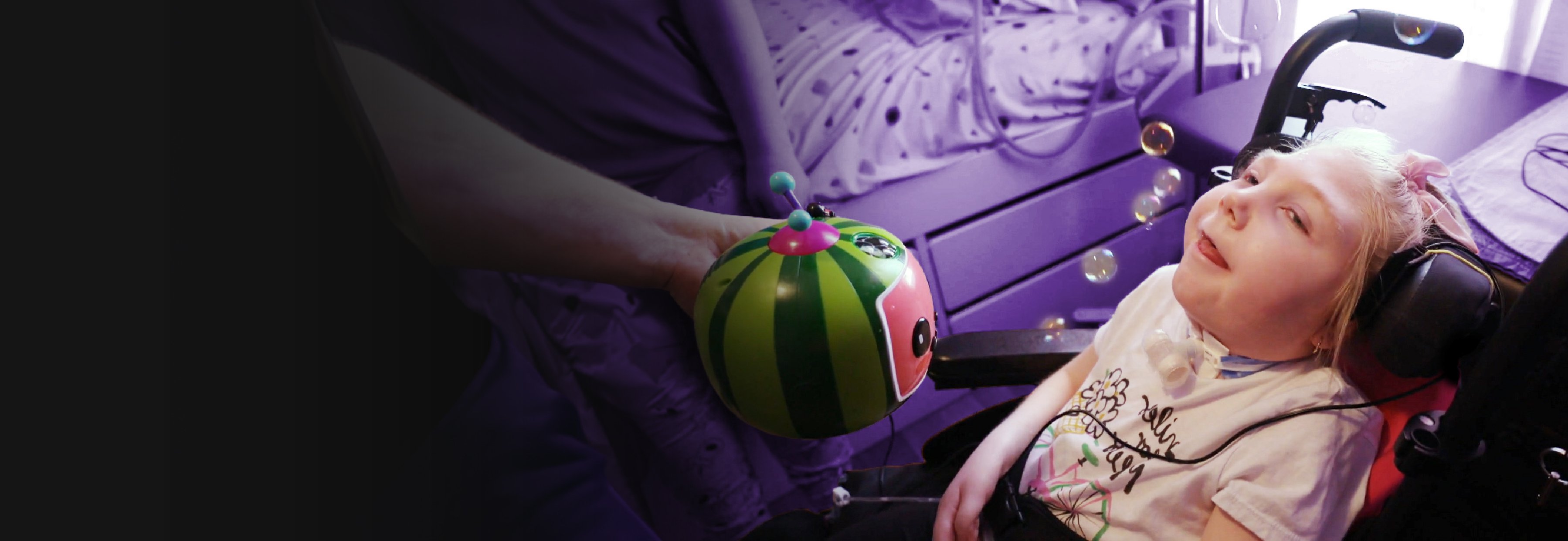 A young girl in a wheelchair looking at bubbles coming out of a coco melon bubble blower