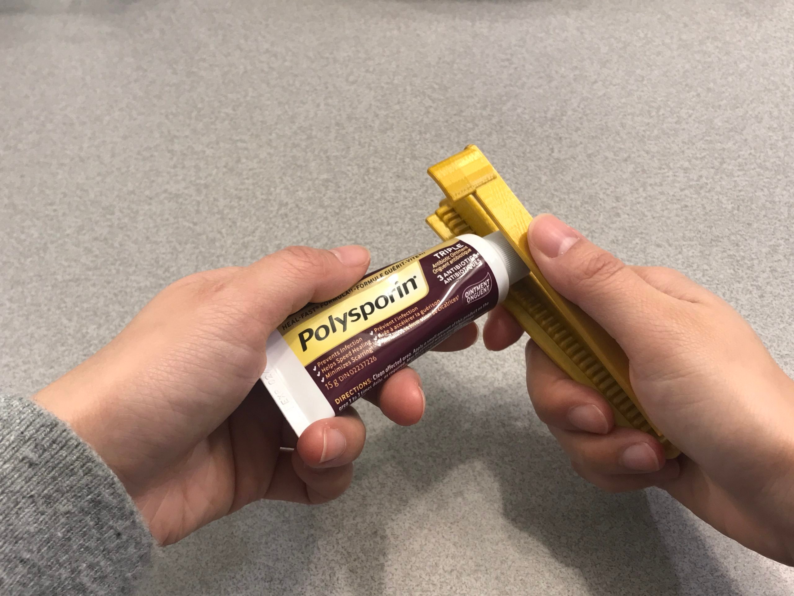 A hand opening a polysporin tube with the tube opener