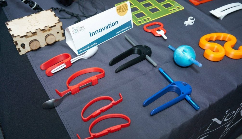 Low tech AT, including the pen ball and bag carrier devices, on a booth table with a sign that says "Innovation."