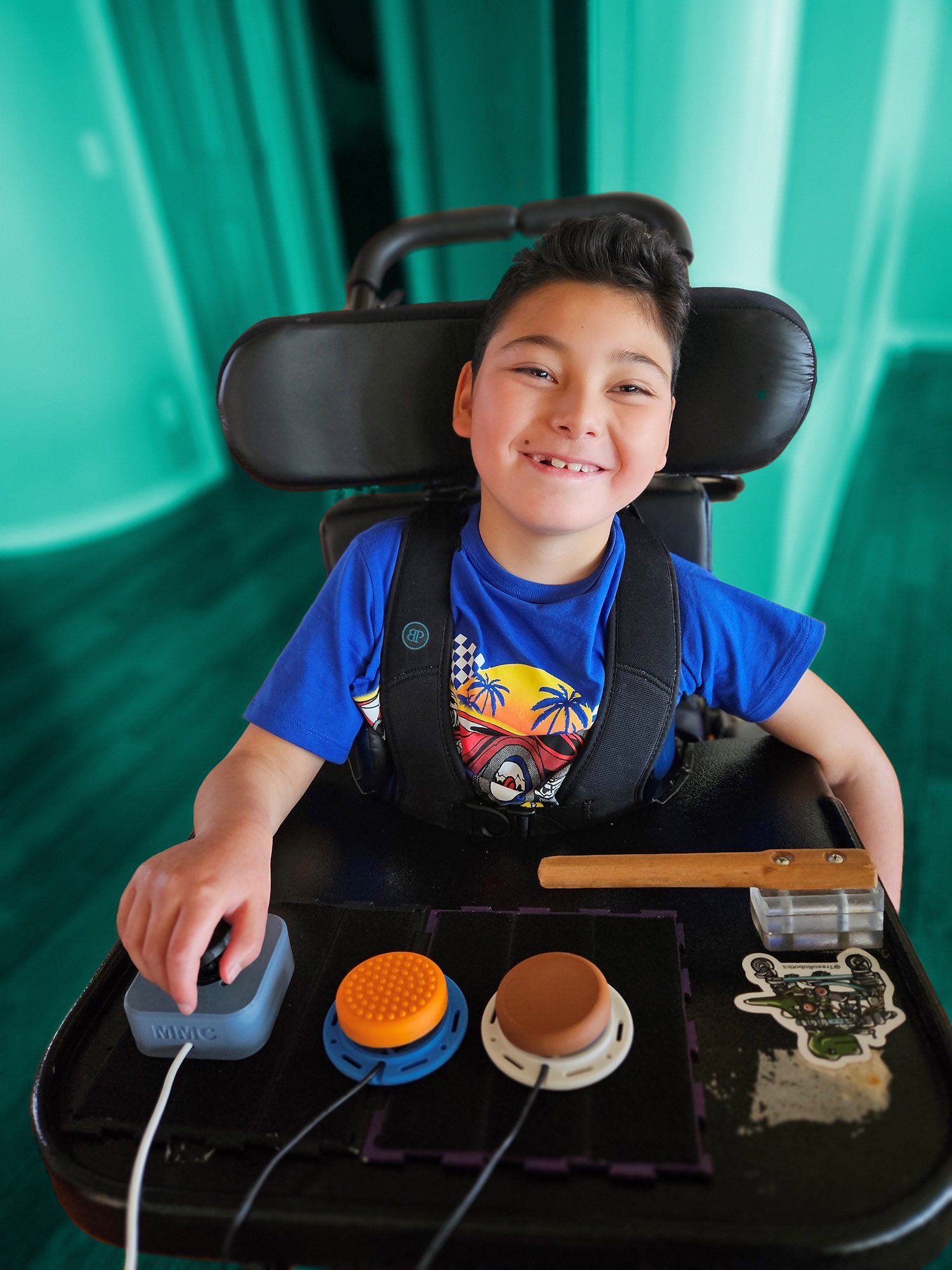A young boy in a wheelchair with a 3d printed joystick and 2 switches in front
