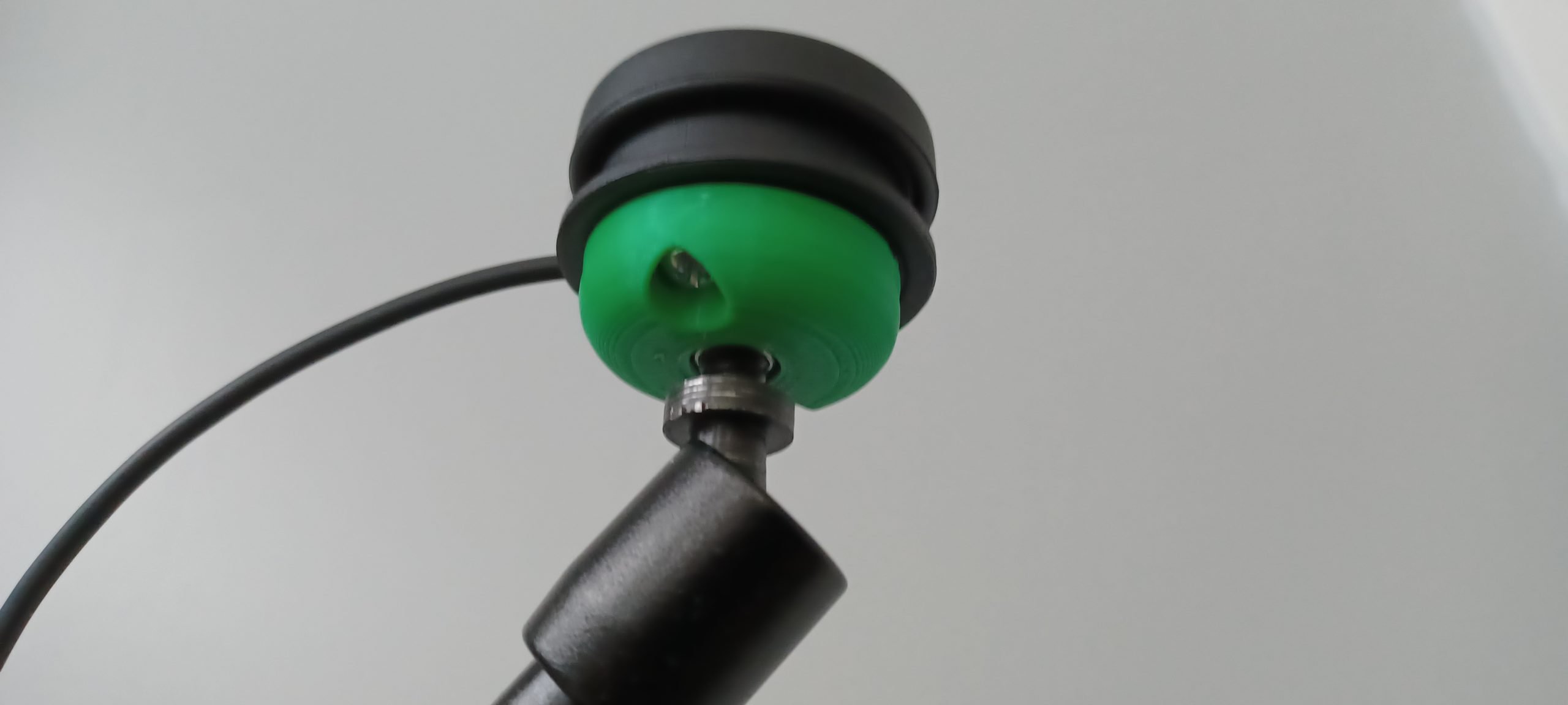 A green 3d printed mounting base attached to a black Logitech small button.