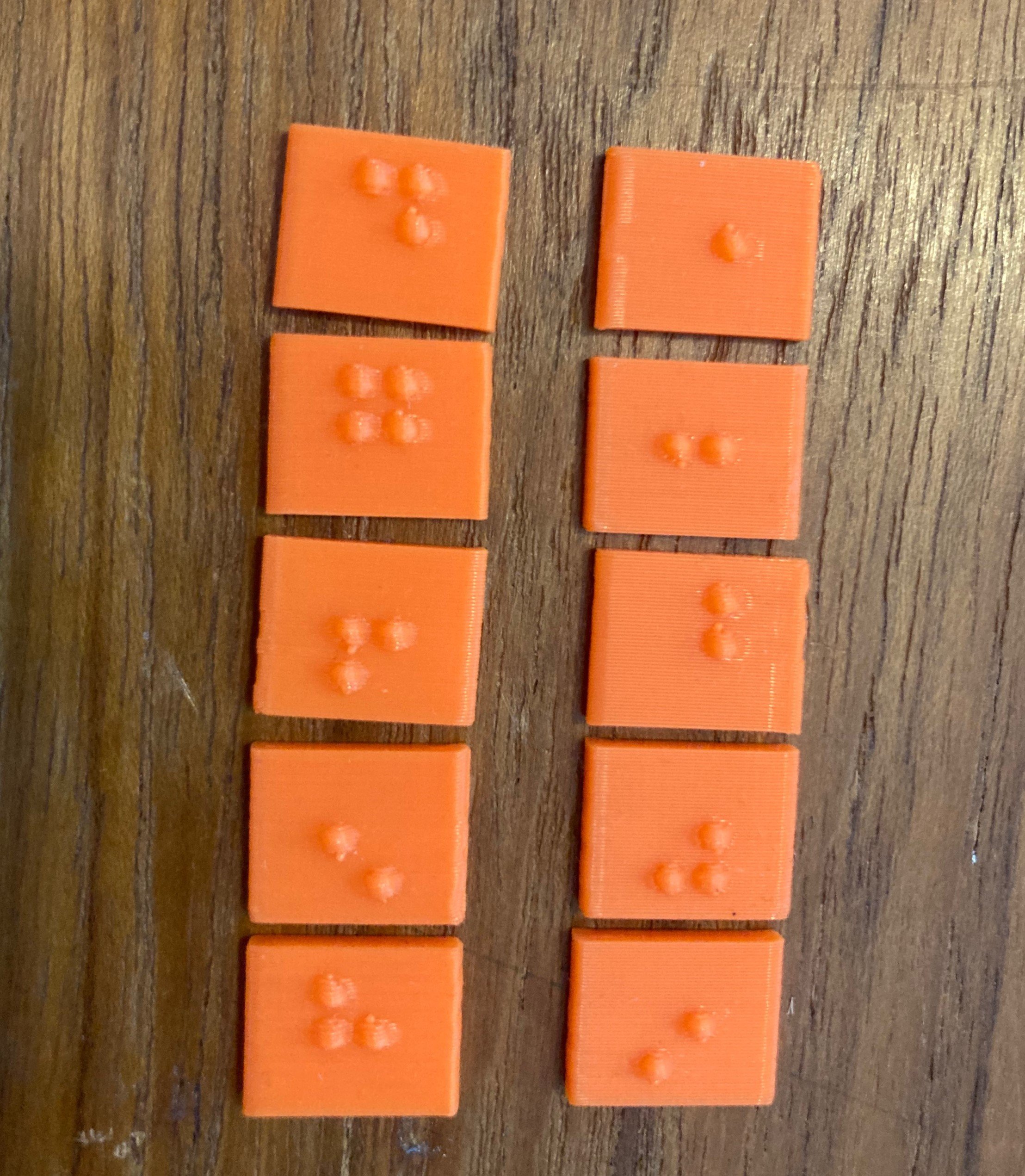 8 3d printed orange braille labels on a table.