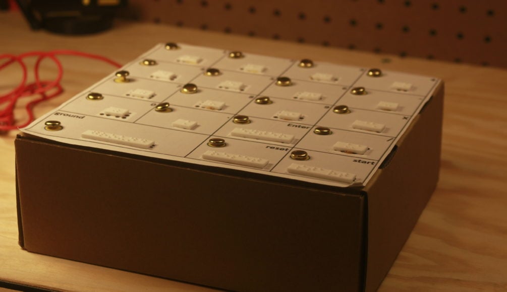 An assembled braille calculator with metal pins and white 3d printed braille labels on a cardboard box.