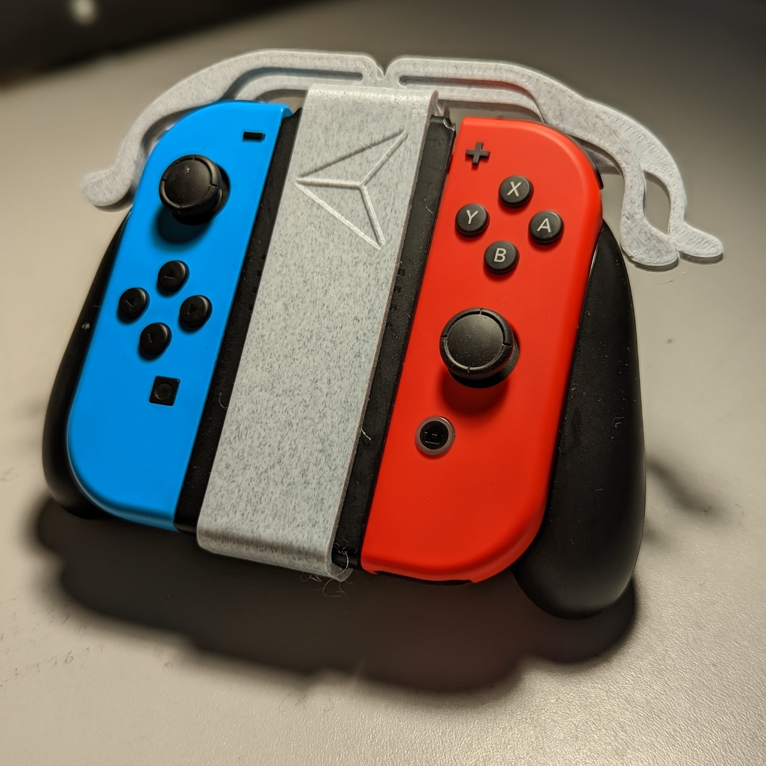 A grey 3d printed intendo joy-con trigger extenders attached to blue and red controllers.
