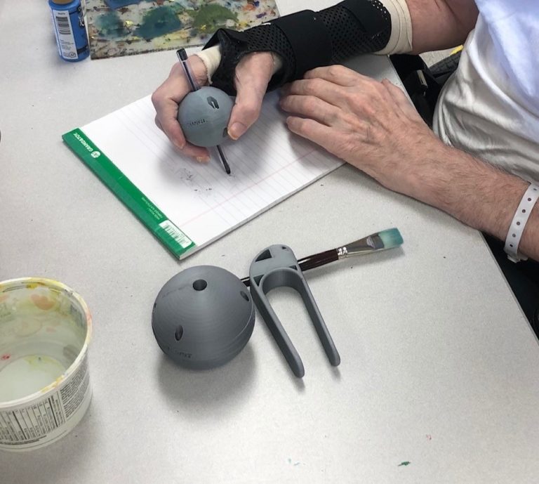 A hand using a grey 3-D printed Pen Ball to write.