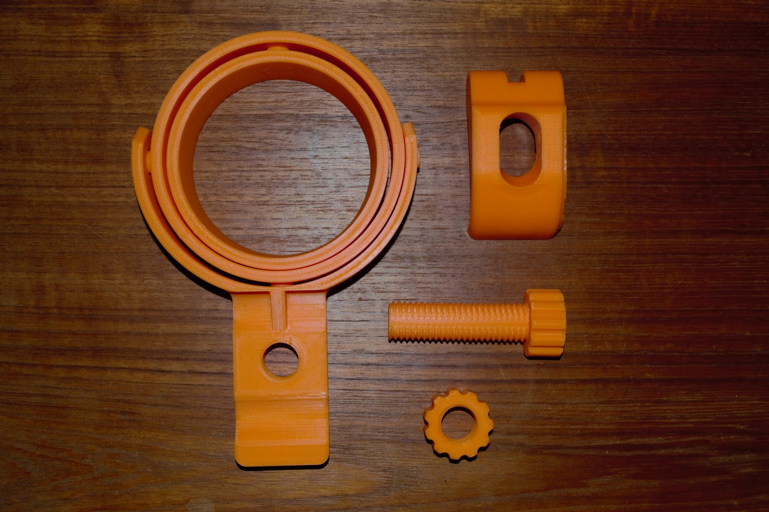 3D printed gimbal, clamp, bolt, and nut laid out on a wooden surface.