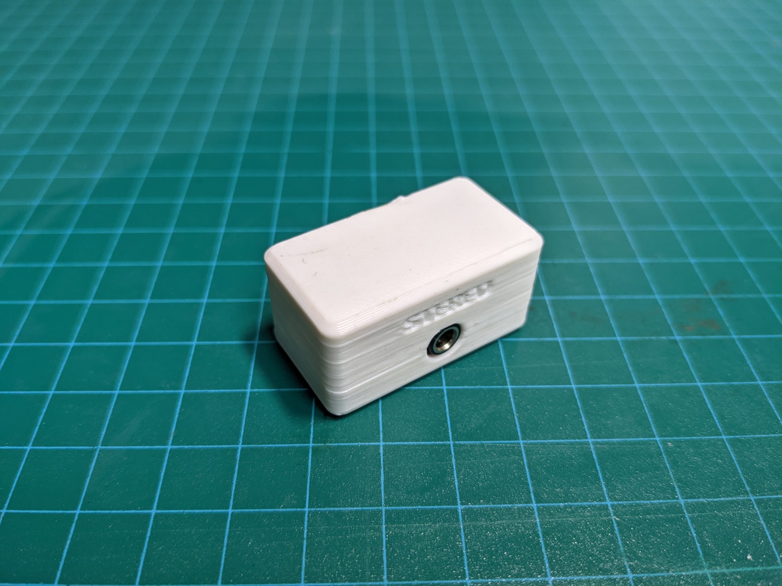 A rectangular 3d printed switch adapter with one mono jack port on a green cutting mat.