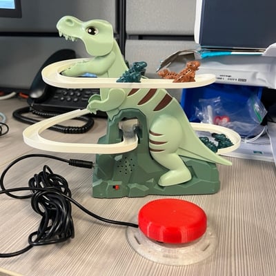 An interact switch plugged into a large, plastic toy dinosaur. There are two small dinosaur sliding down a sloped race track that wraps around the large dinosaur.