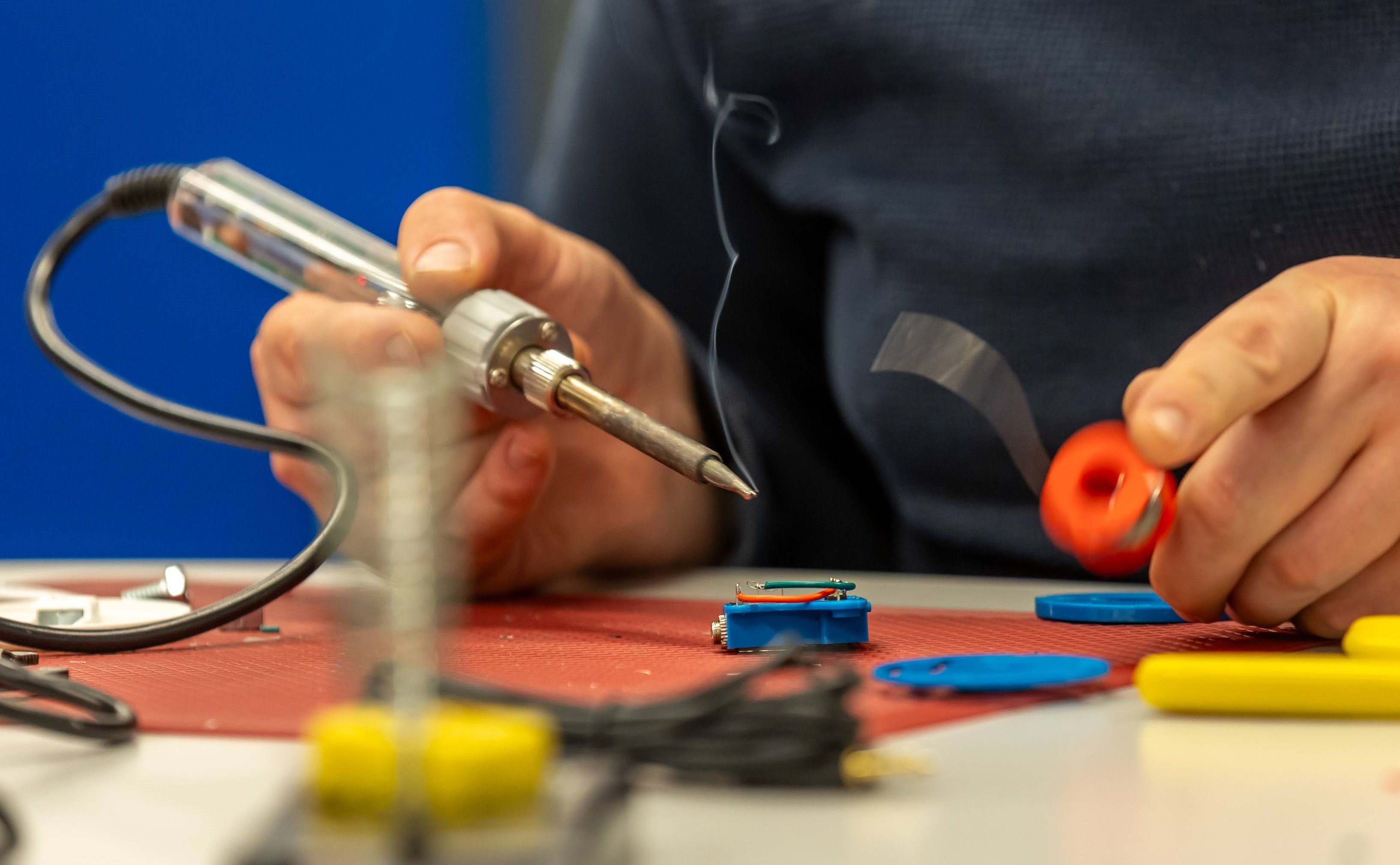 A close up of an individuals hands holding a soldering iron and solder.