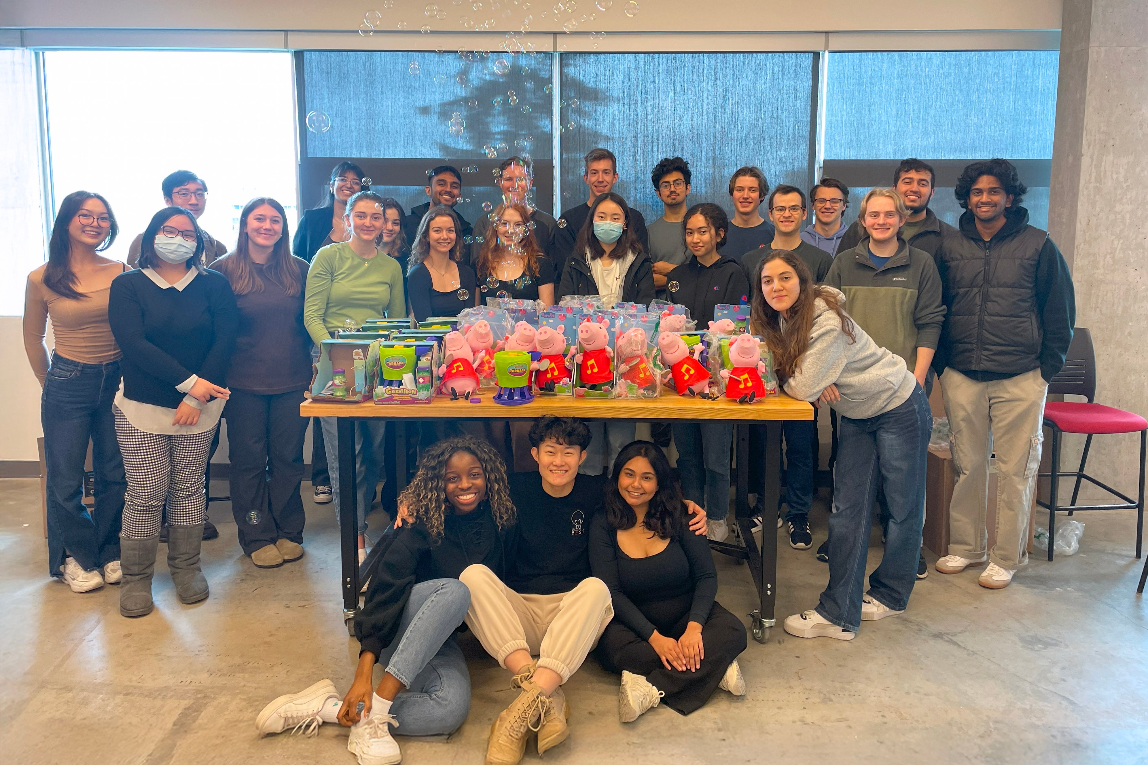 A large group of university students standing around a table with various adapted toys.