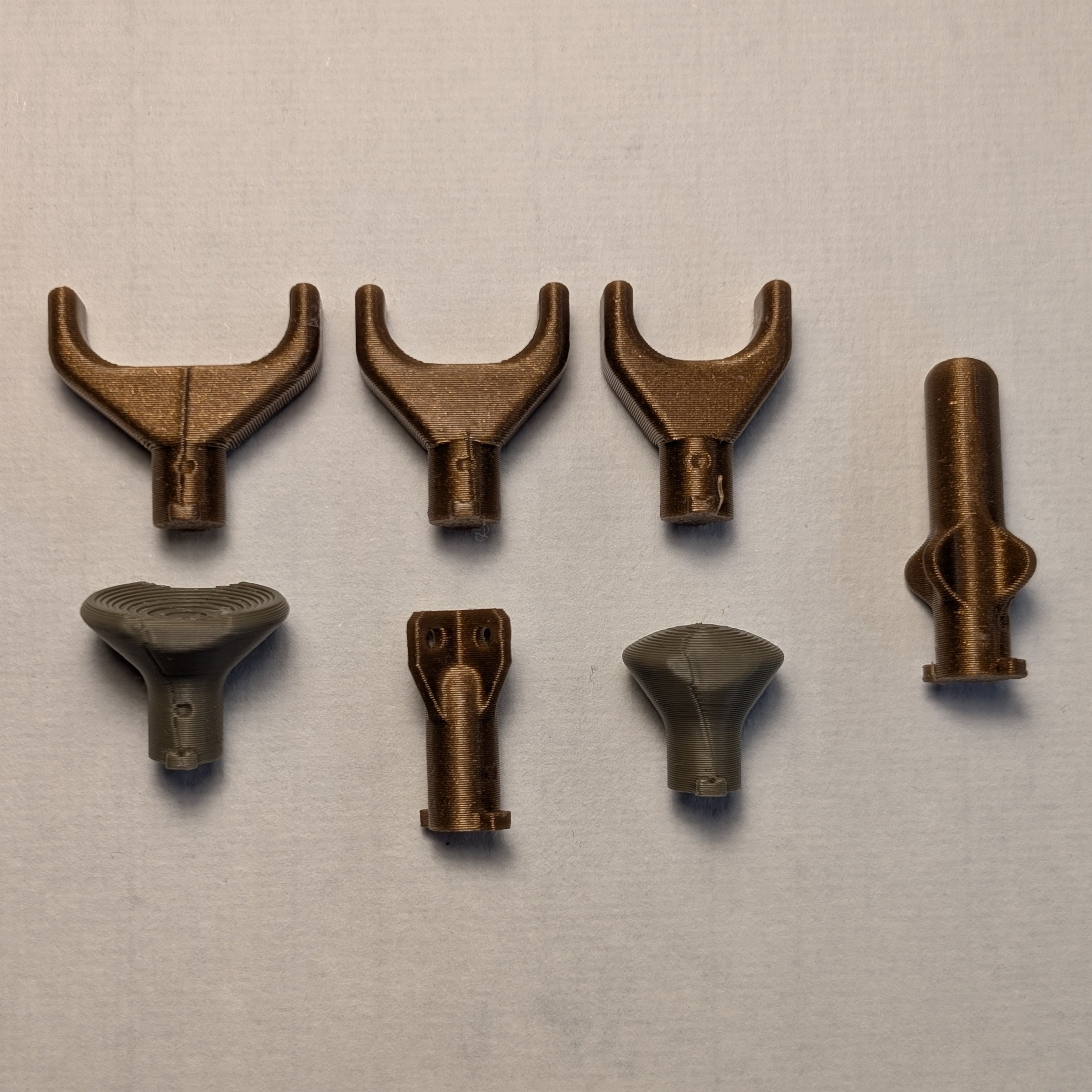 The willow joystick toppers on a white background. All three goalpost toppers, the stick topper, and the mouldable topper are printed in gold, and the concave and convex toppers printed in green.