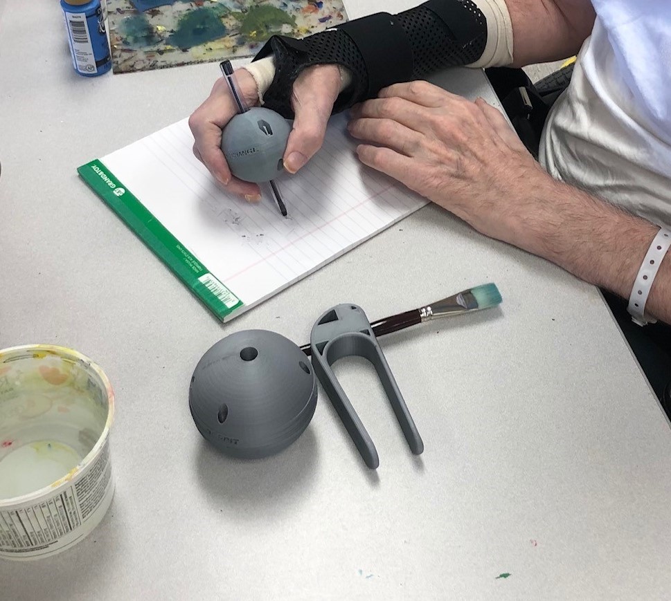 A person wearing a black hand brace using the grey, 3d printed pen ball to write