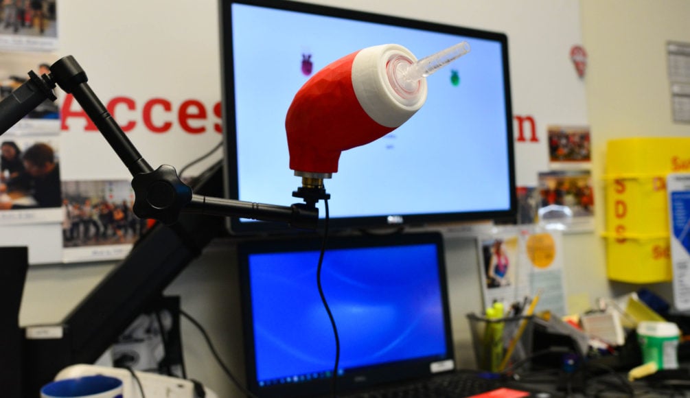 A red LipSync device in front of a TV and computer display.