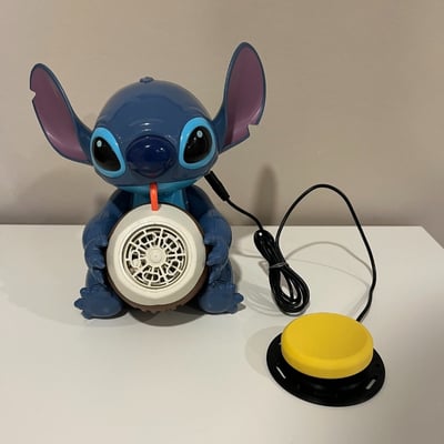 An interact switch plugged into a bubble machine shaped as the Stitch character drinking from a coconut with a straw
