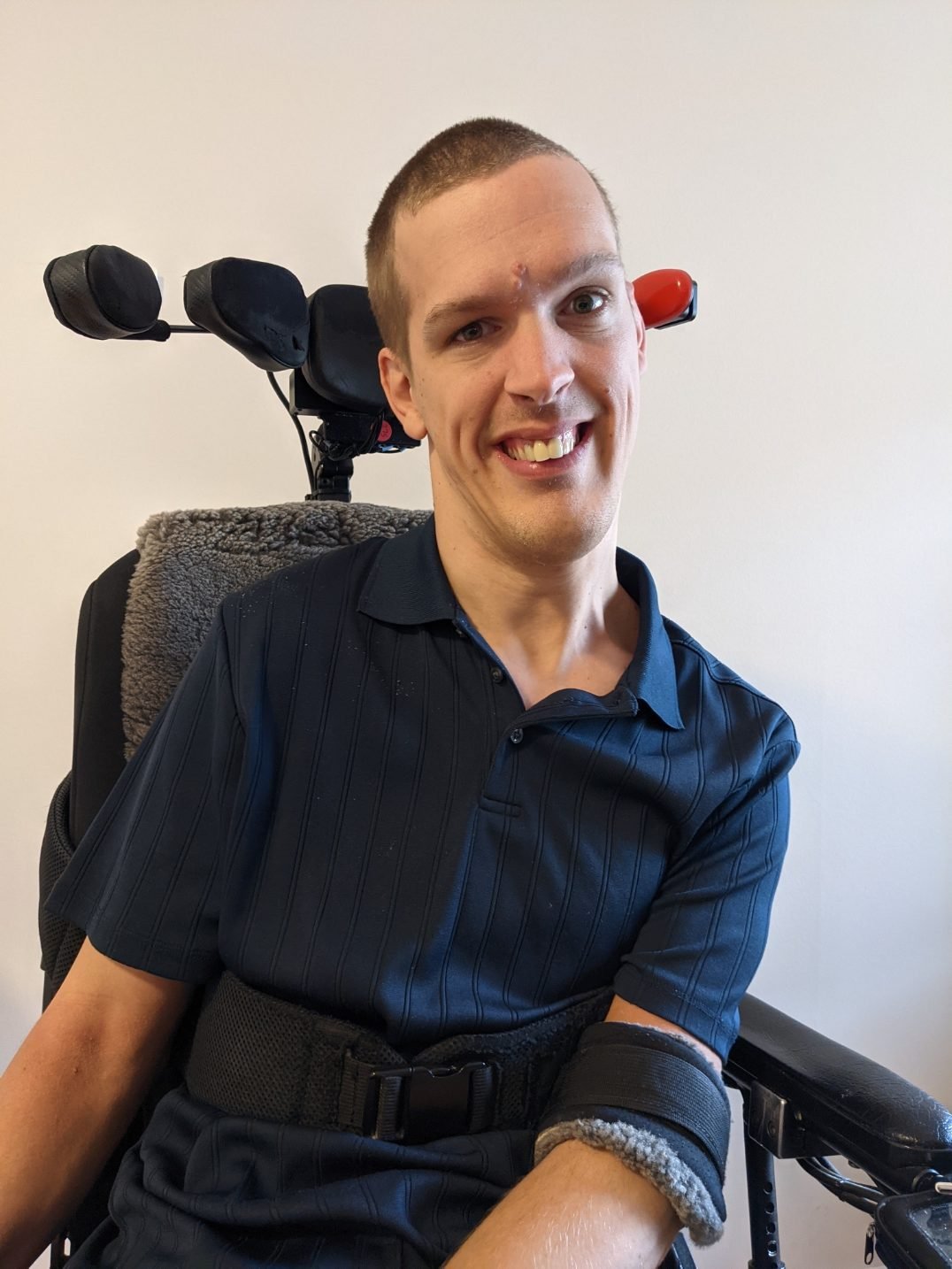 A man with short cropped hair and brown polo in a wheelchair