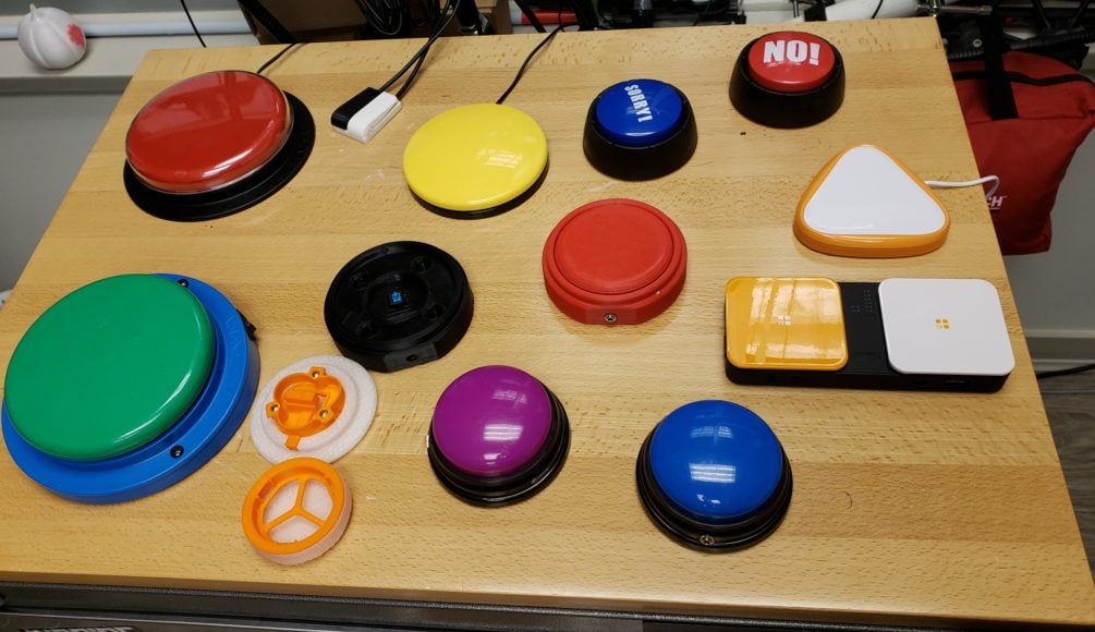An assortment of different assistive switches in different colours and shapes on a wooden table.