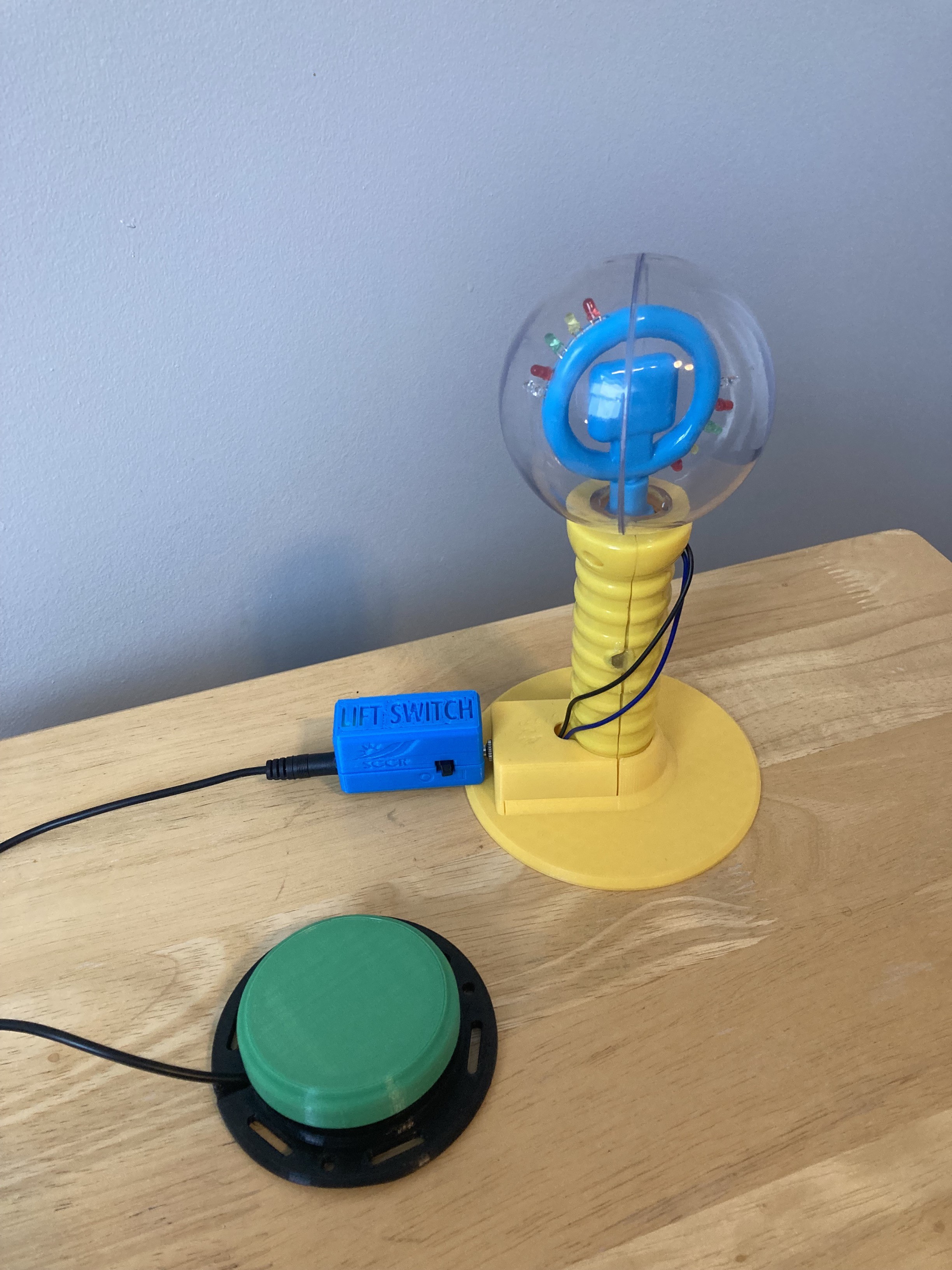 Photo of the Lift Switch with a yellow spinning light wand toy, with a green assistive switch plugged into it.