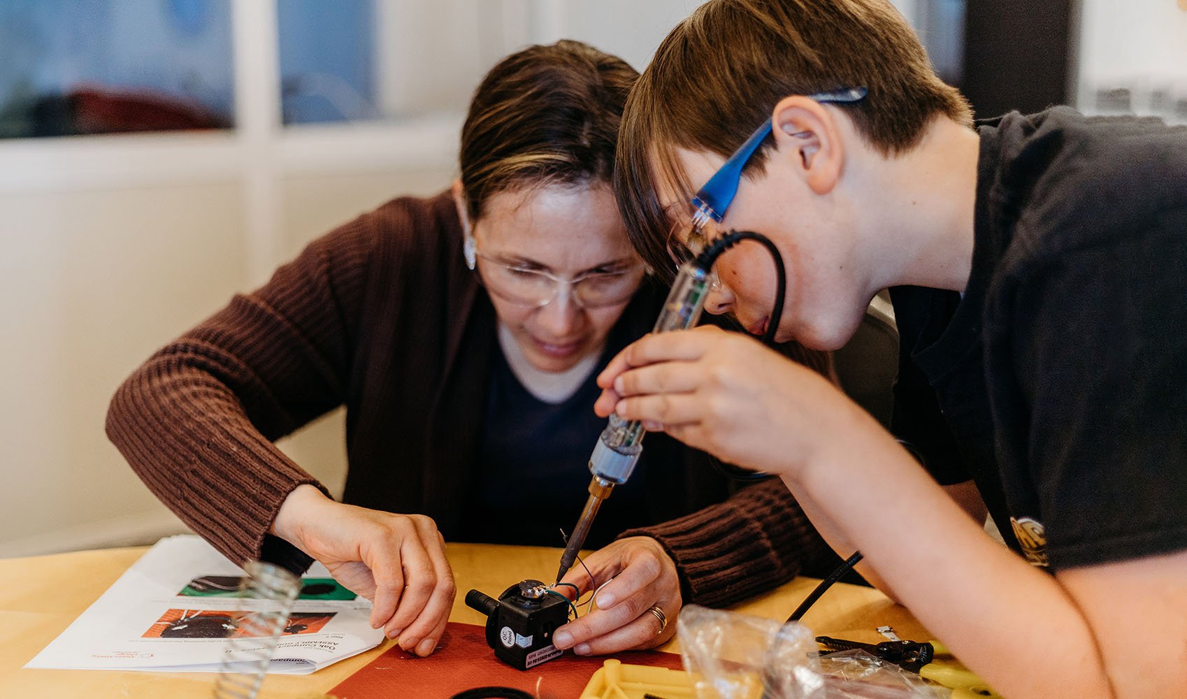 A teacher helping a student solder a joystick.