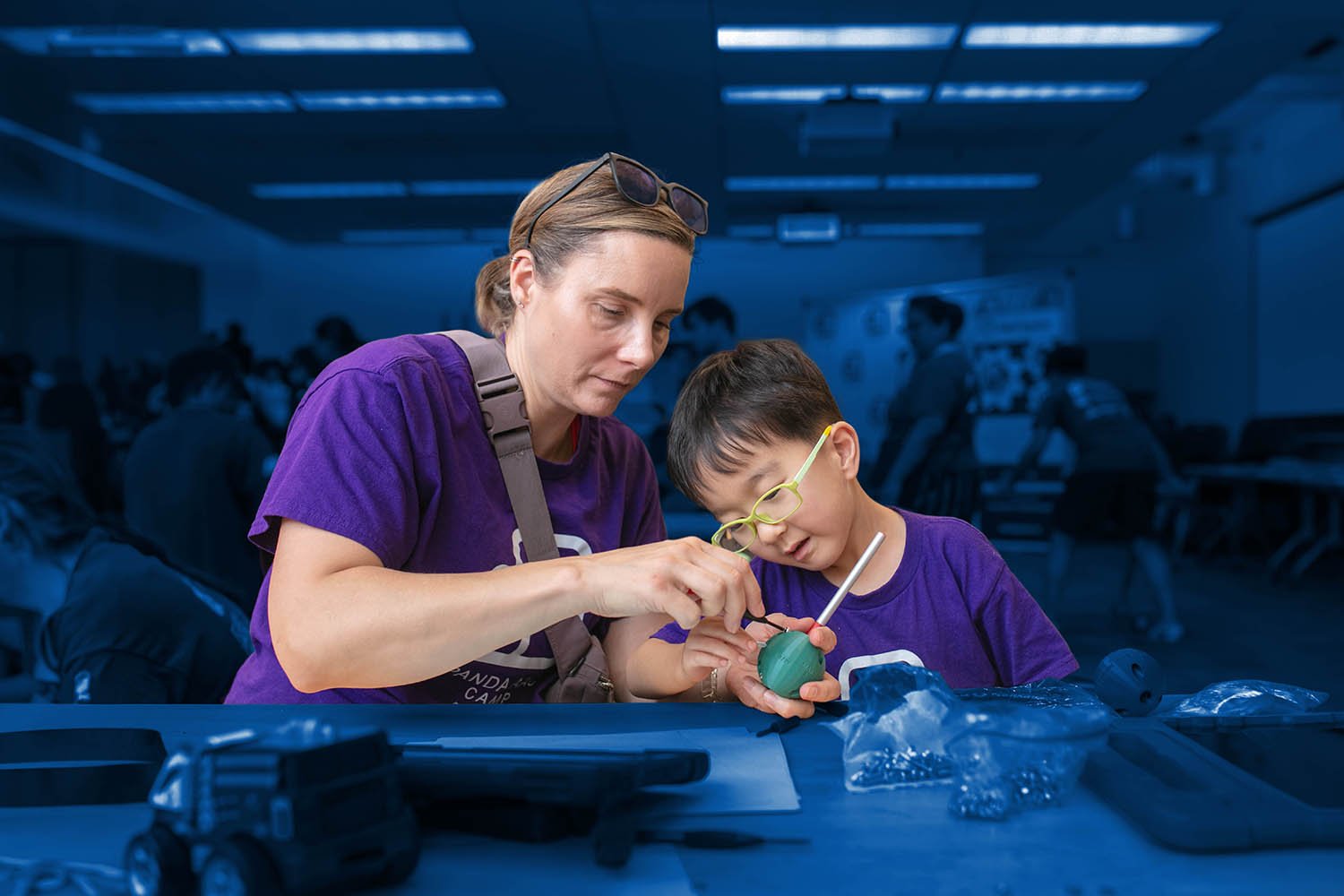 A woman assembling a writing aid with a young boy looking closely at the assembly.