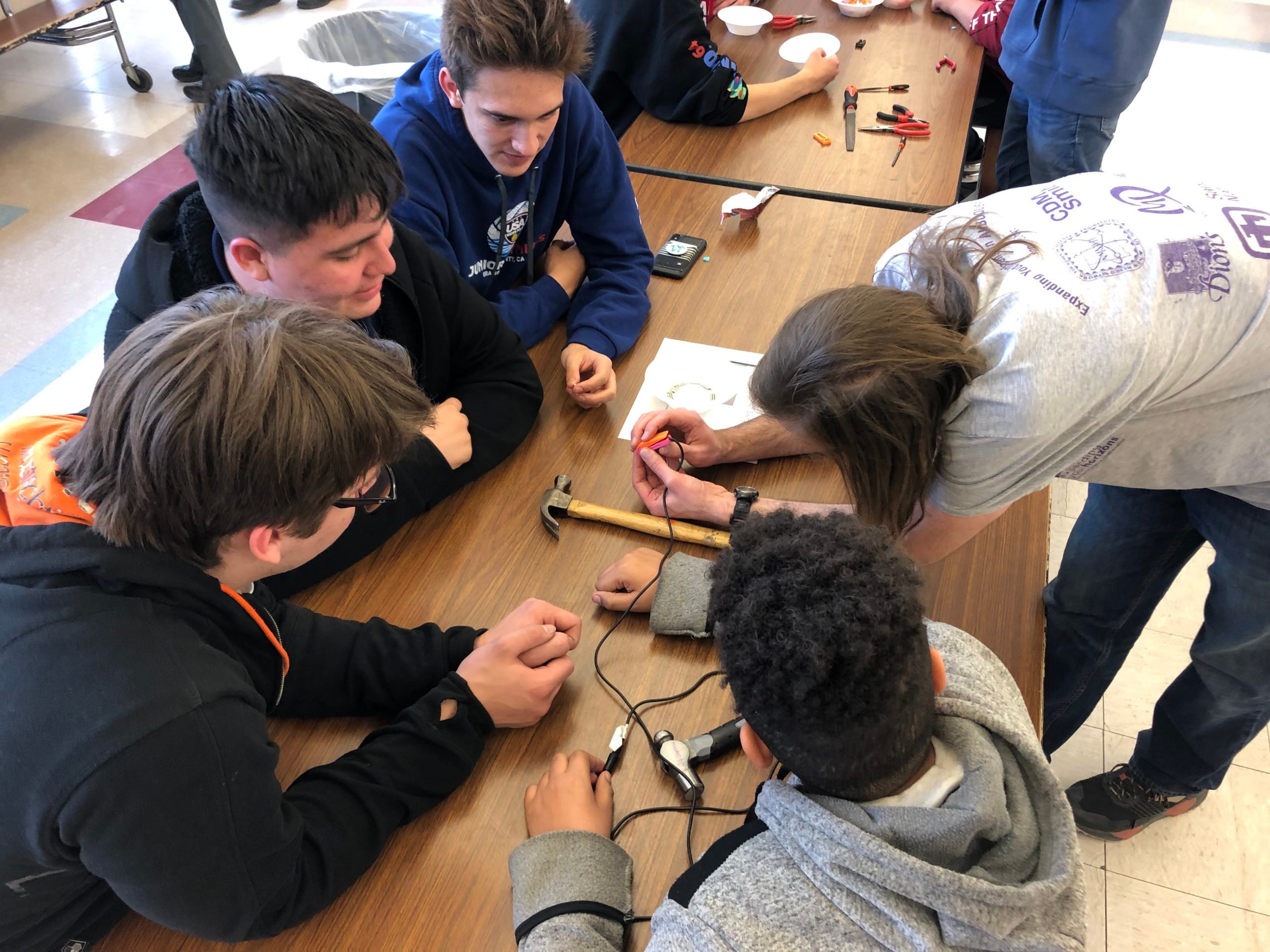 Volunteers at Bosque School leaning over a table examining tools and electronic components.