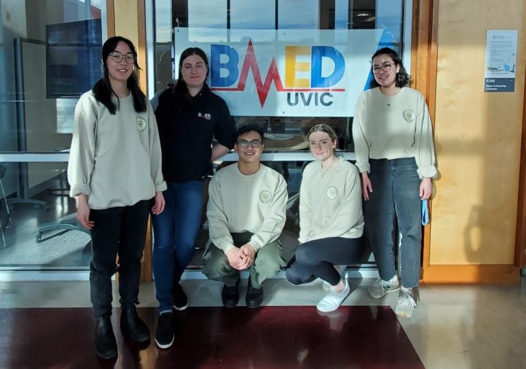 University of Victoria student club posing in front of a poster that says BMED UVic