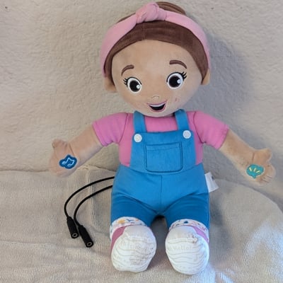 Two cables connected to a plush doll shaped as the Ms Rachel character