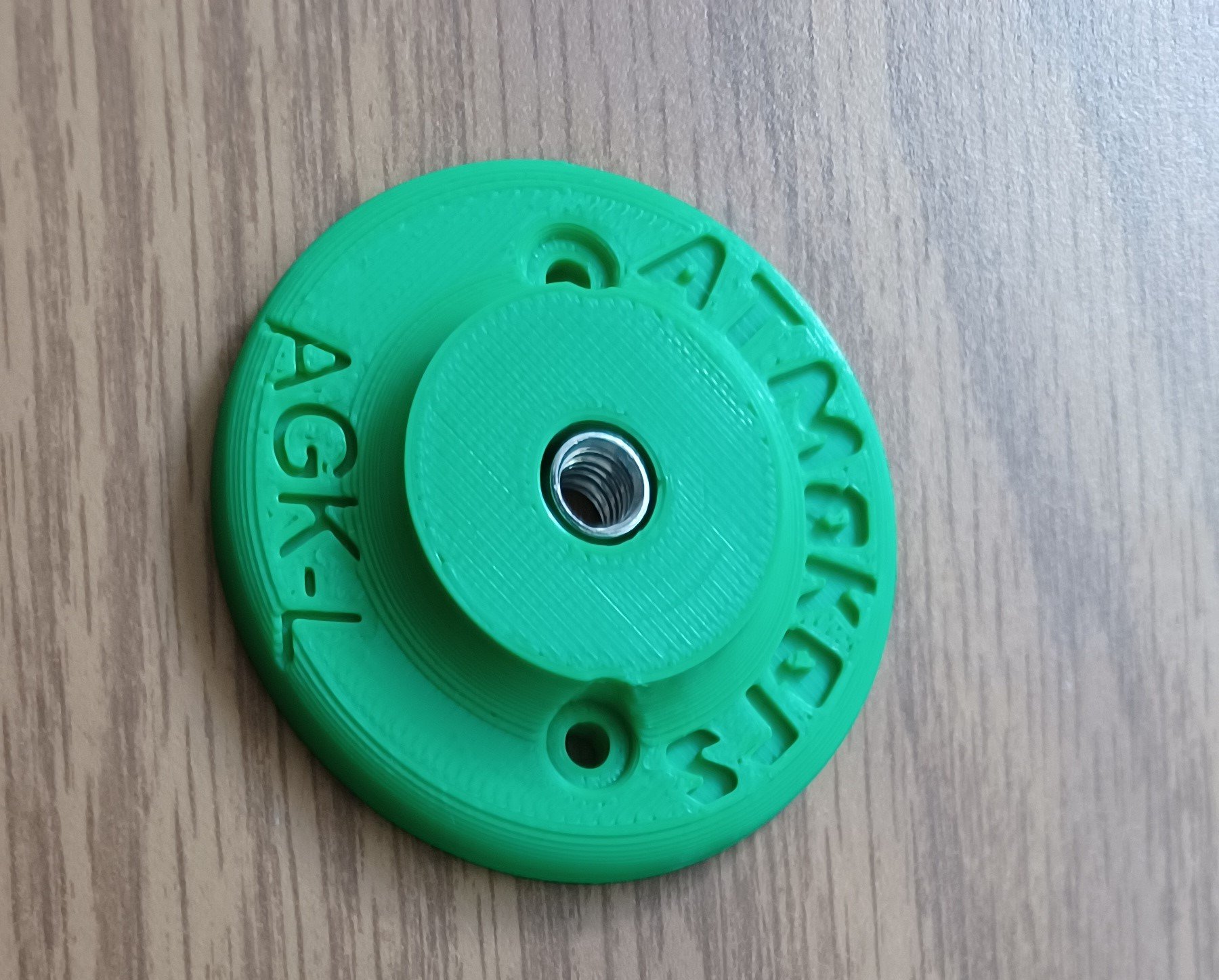 Green 3d printed large button with a t-nut inserted on a wood background.