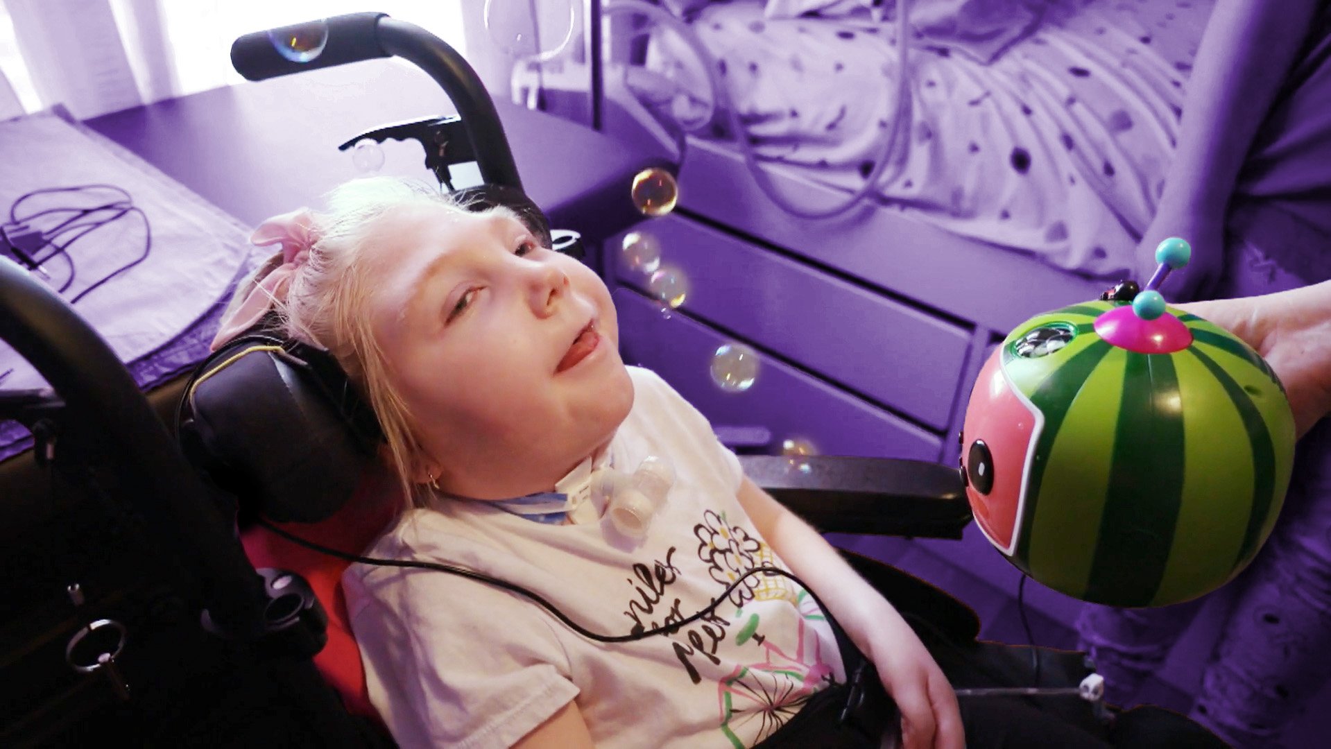 A young girl in a wheelchair looking at bubbles from a coco melon bubble blower