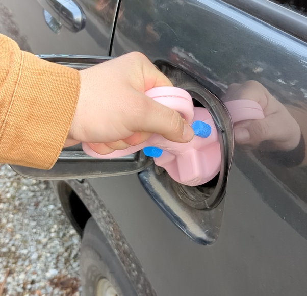 A hand holding the gas cap opener over the gas cap of a grey car