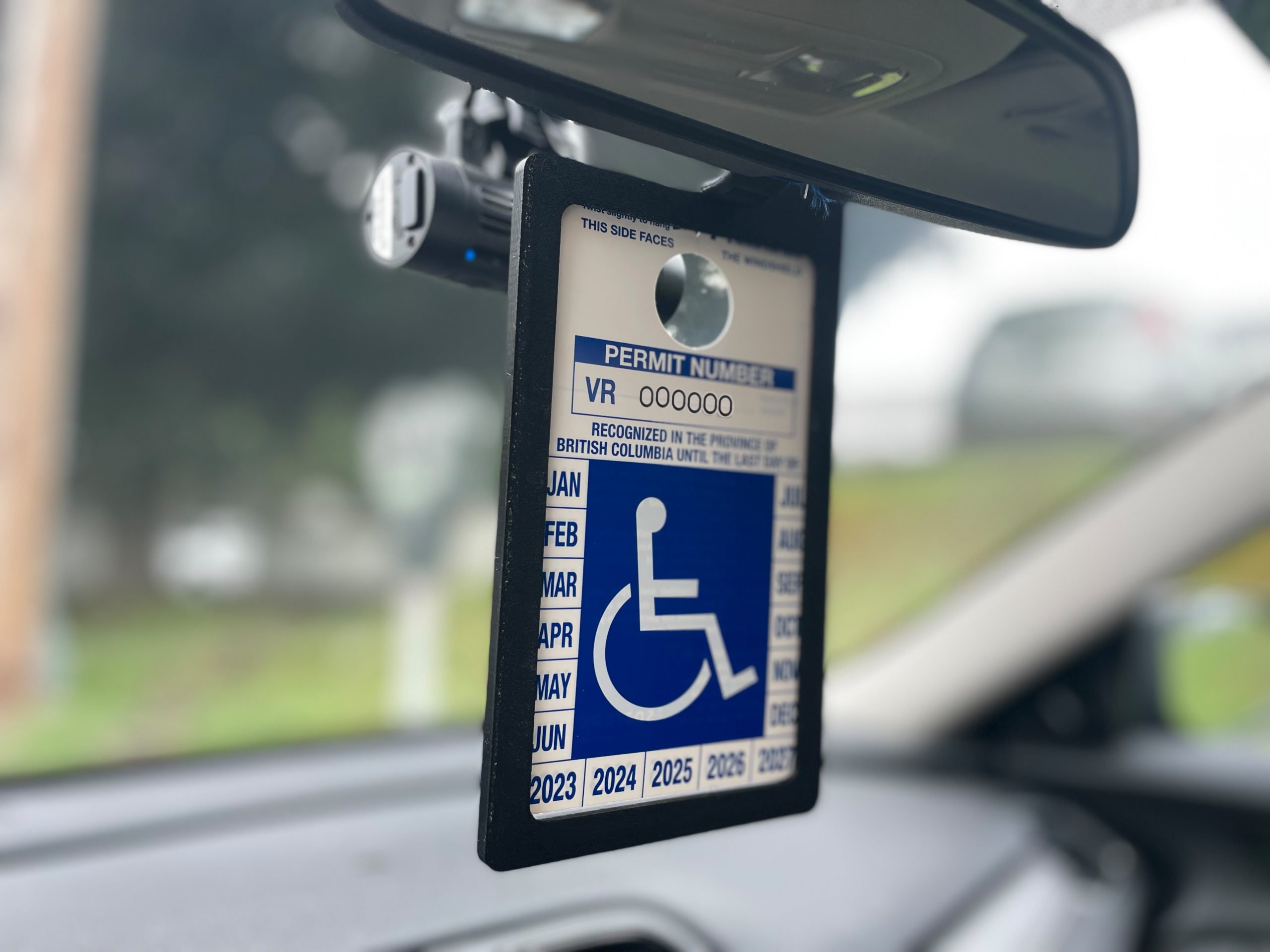 A black 3d printed permit holder hooked on the back of a rear view mirro with an accessible parking permit inside.