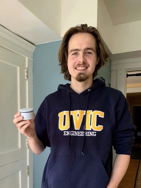 A man with long brown hair and UVIC sweater holding an assistive switch.
