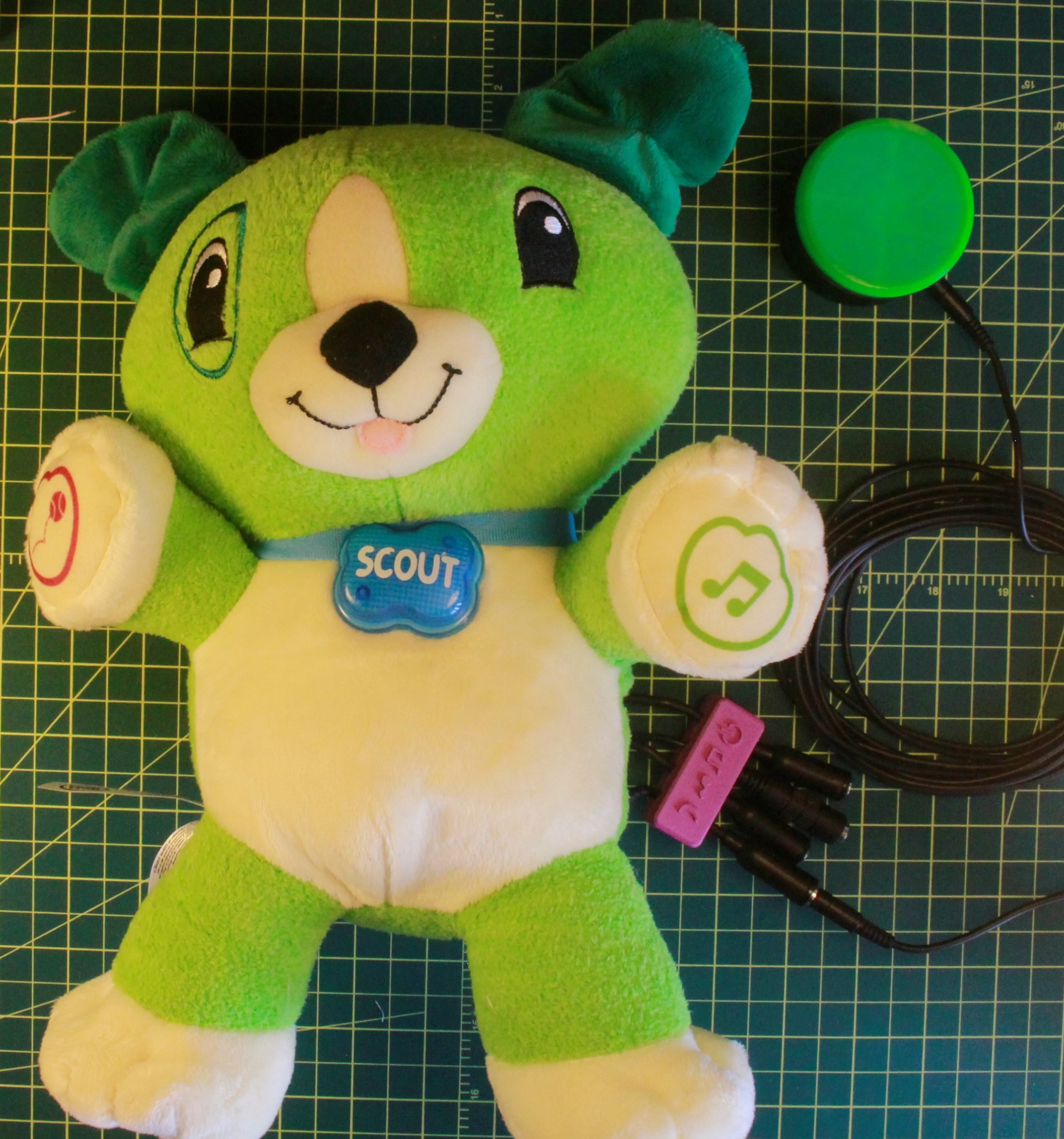 A green switch adapted toy dog with 4 mono jacks and a green 3d printed assistive switch plugged in.
