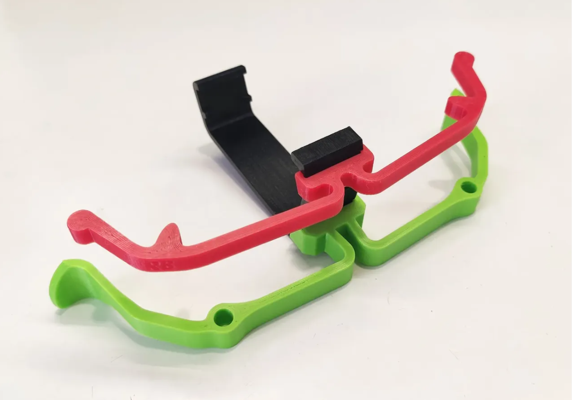 Red, green, and black 3d printed extenders for the Xbox One controller on a white surface.