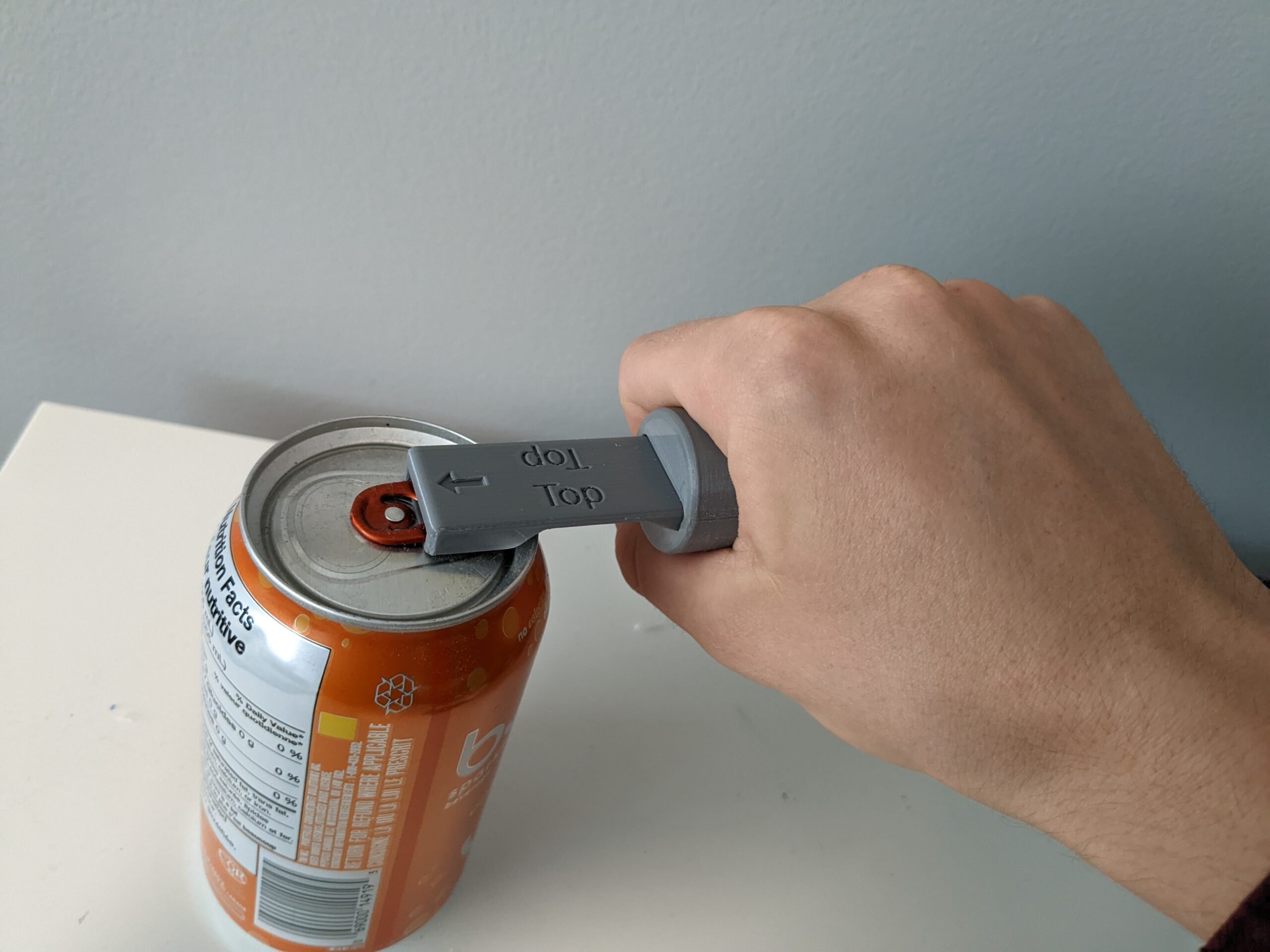 A hand holding a 3D printed can opener with cylindrical handle to open a pop can.
