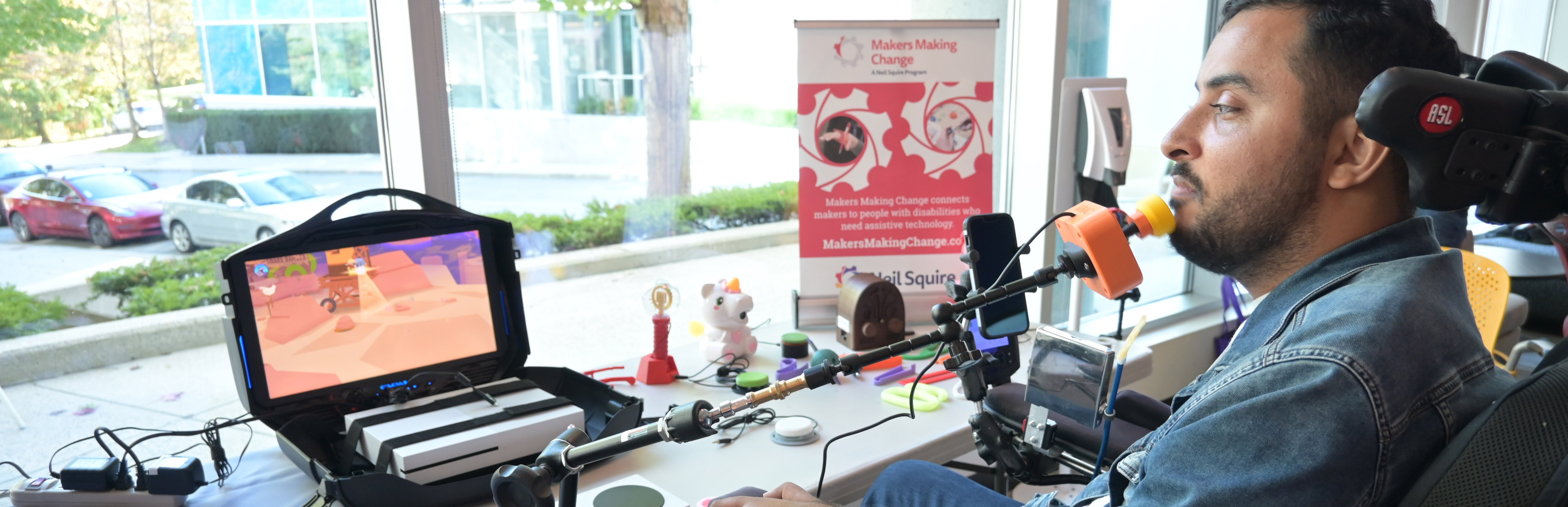 A person in a wheelchair using a chin switch to play a video game. on the table are other assistive devices.