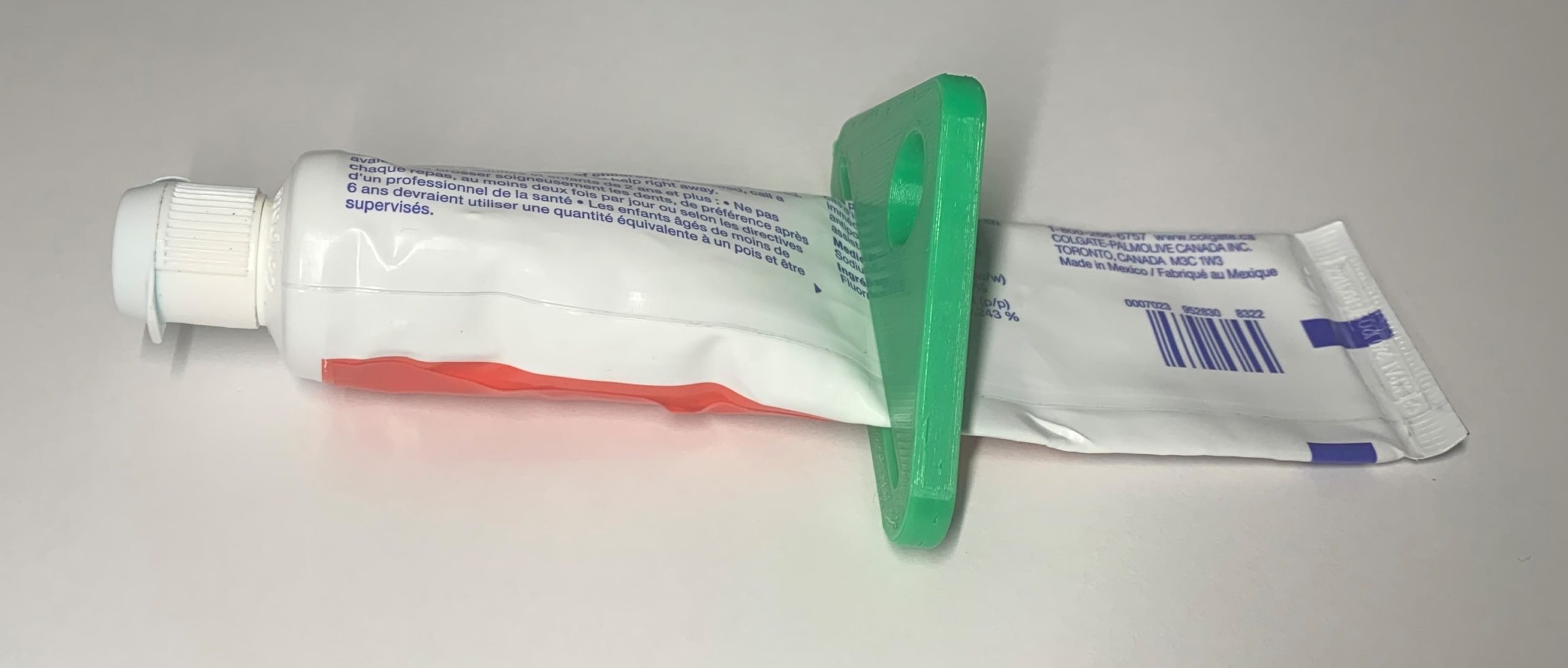 A green 3d printed Toothpaste Squeezer device slid halfway up a tube of toothpaste.